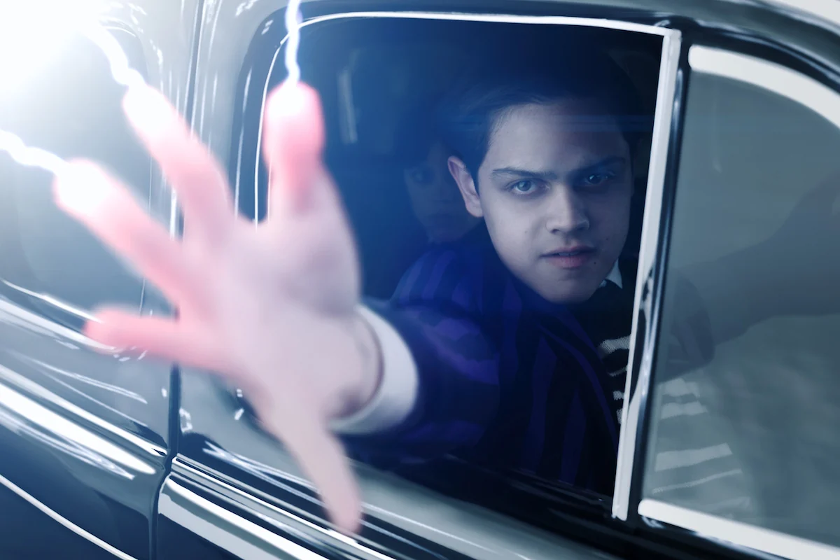 Isaac Ordonez as Pugsley Addams reaches through a car window in a Wednesday Season 2 still on Netflix